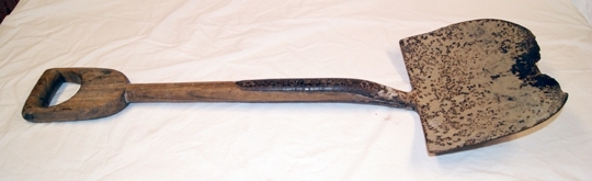 Spade. Jernskoning og avrundet blad. Slitt. Handtak og skaft i tre (eik). Gripetaket reparert med gjennomløpende jernbolt. Innskåret initial og tall: A.E. 1918