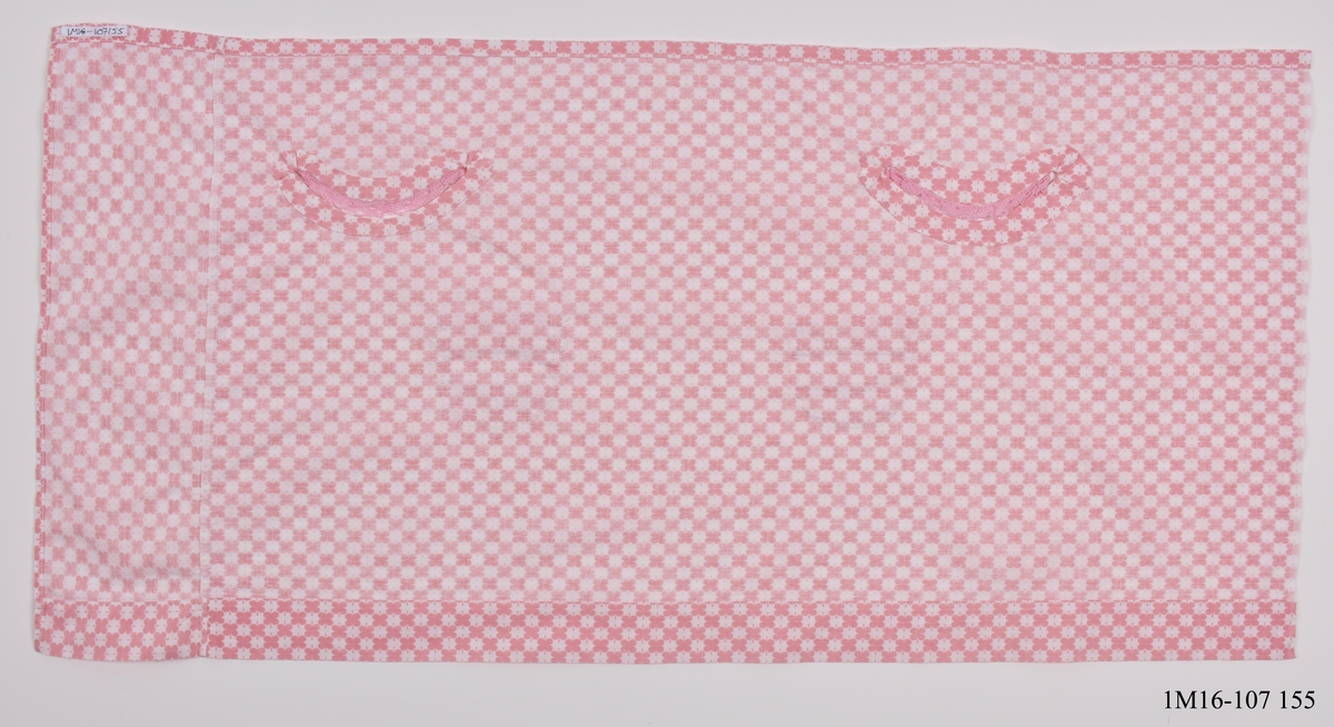 Klänning, vit botten med rosa fyrbladsformat mönster.  Holkärmar med rosa spetskant.  Rak halslinning som dras ihop med hjälp av ett bomullsband så ringningen rynkas, banden knyts sedan baktill. Bandet saknas. Två fickor fratill med rosa spetskant i överkanten.  Ej färdig, knappar saknas.  Rektangulär i formen. Sydd i hemmet på symaskin.