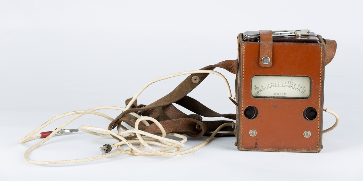 Voltmeter i læretui.To kabler med krokodilleklemmer. Måler også Ohm. Brunt etui, sort måleinstrument.