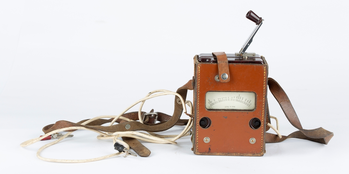 Voltmeter i læretui.To kabler med krokodilleklemmer. Måler også Ohm. Brunt etui, sort måleinstrument.