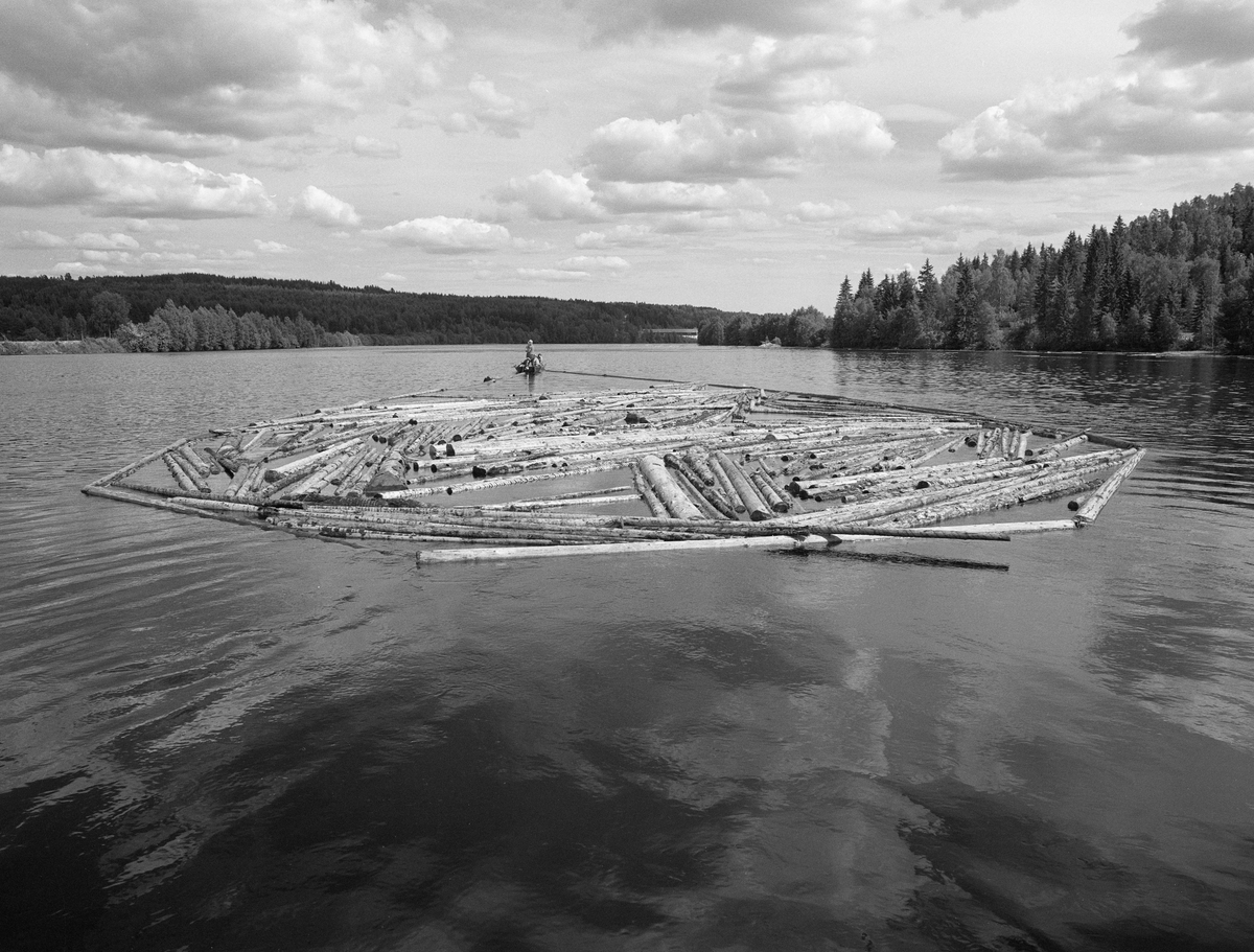 Sluttrensk i Glomma i juni 1985. Dette var det siste året det foregikk ordinær fløting i dette vassdraget. Fotografiet er tatt mellom Hanstadfossen og Skjefstadfossen i Elverum kommune. I forgrunnen ser vi en tømmerbom – en ring av tømmerstokker som var kjedet sammen ende mot ende til en ring – som løstømmer som lå igjen etter hovedfløtinga kunne samles i. Her slepes en slik tømmerbom nedover vassdraget ved hjelp av en fløterbåt med påhengsmotor.