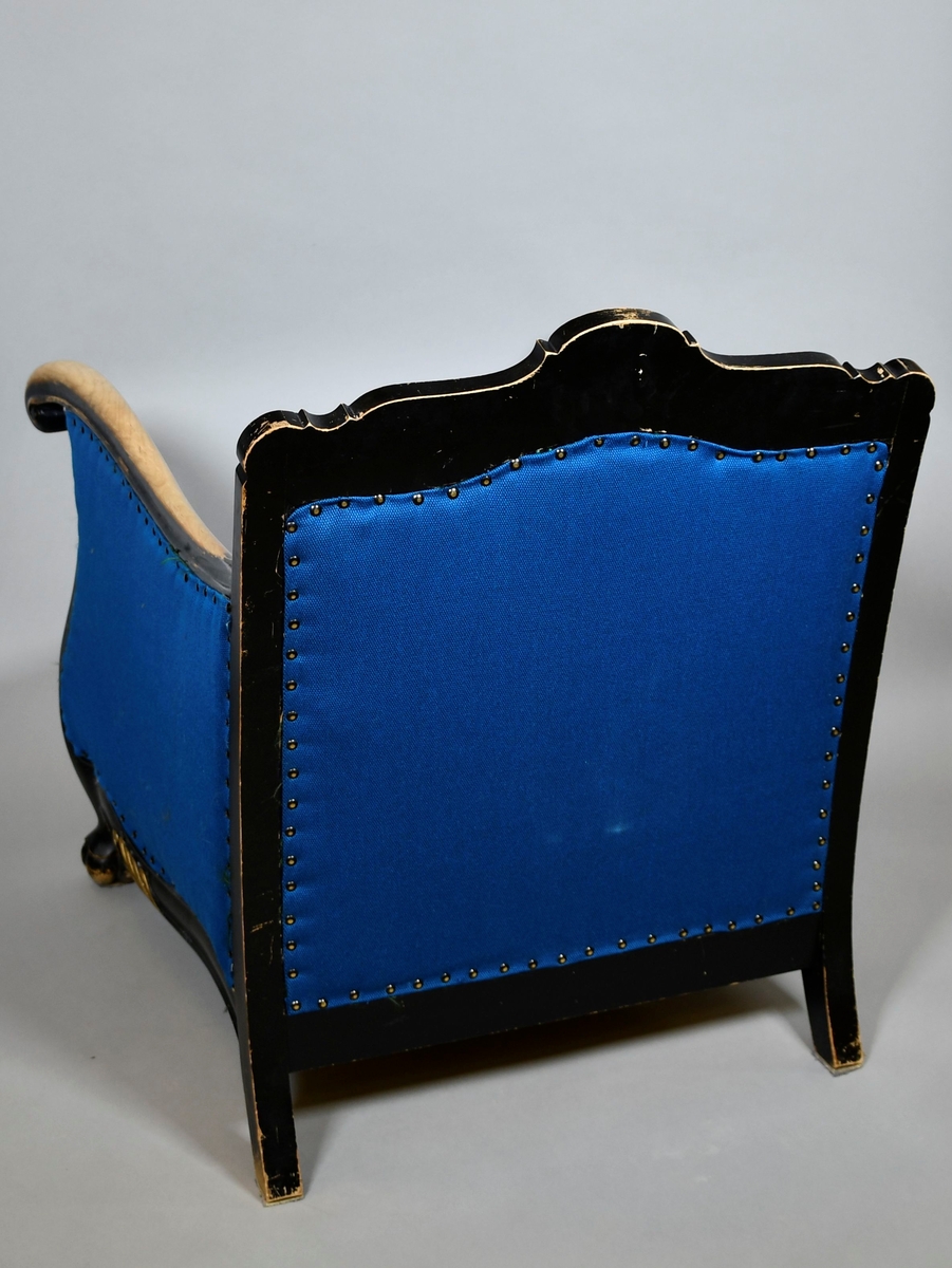 Barokkinspirert lenestol. Treverket har svart grunnfarge som er avslitt flere steder, spesielt på armlenene. Toppen av ryggen har symmetrisk skåret dekor av akantusranker, og et stående skjell i midten. Randen har bølgete form. Armlenene har kurvet form, og nederst på håndtakene er det volutter. Sprossen under setet har liggende skjell med to volutter på toppen. Treskåret dekor er gullfarget. Stolen har nytt, blått trekk.