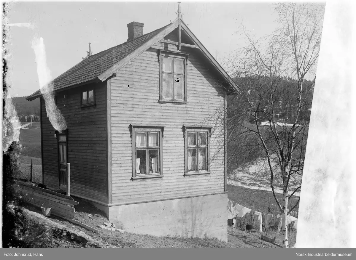 Bolighus i Hvålagata, jorder i bakgrunnen. Klær henger til tørk foran huset. 