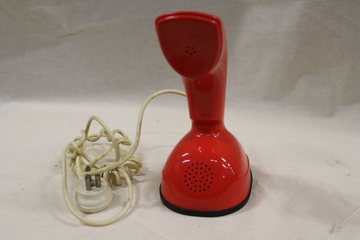 Rød teleofn med tall-dreieskive og summetonebryter under på foten. Ledning går ut fra baksiden på bunnen. Formen på telefonen kan minne om hodet på en Kobraslange.