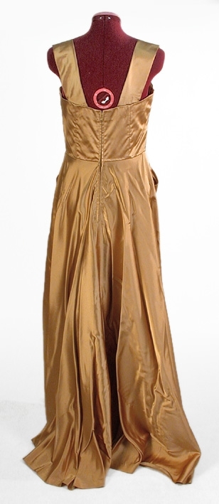 Klänning av guldfärgat atlassiden.
Liv: Kupformat liv med lagda veck mot överkanten. 4 st små släta våder, kilformat mellan kuporna. 2 st breda axelband med 1 veck i framkanten. Bystdelen 2 st lagda veck. Insydd bysthållare. Bakstycket i 4 st släta delar med insyningar. Hänghällor under ärmarna. Livet fodrat med vitt tätvävt bomullstyg. 6 st insydda spiraler.
Mått i cm: Axellängd 37, bredd 7.
Kjol: 2 st raka våder framtill. Slät mitt fram med ett stort fickliknande veck samt ett litet veck på var sida framstycket. Bakvåden snedklippt med mycket vidd samt släp. 36 cm långt blixtlås baktill. 
Mått: Kjolvidd 452 cm.