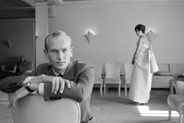 Porträtt av en man i interiör med en stående kvinna i bakgru