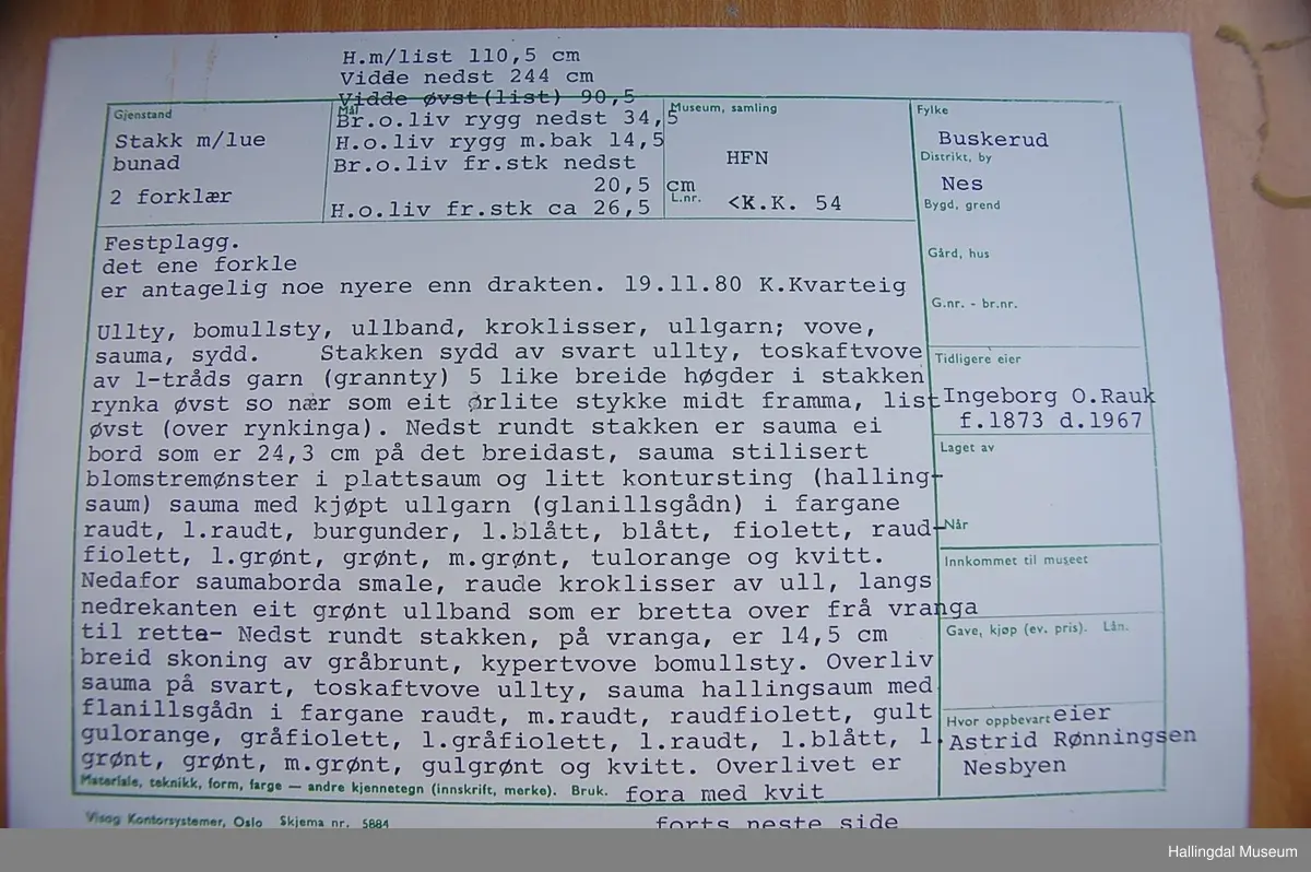 Frihåndsbrodert festbunad fra Nedre Hallingdal. Stakken er sydd av svart ulltøy, toskaftvevd av 1-tråds garn (grannty). 5 like brede høyder i stakken som er rynket øverst så nær som et ørlite stykke midt framme. På stakken er festet ei list øverst. Fyldig hallingsaum-broderi, akantusranke med 11 roser som er brodert rett på stakken. Over akantusranken er det broderte greiner som står loddrett på en brodert grønn rett bord. Nederst på stakken er det en slitekant av grønt ullbånd som er brettet inn på baksiden. Over denne er det røde kroklisser. Stakken er skonet med et gråbrunt kypertvevd bomullstoff.  Overlivet er foret med hvitt bomullslerret, en ørliten stikklomme (h. 7 cm, br. 4,7 cm) på innsiden av det ene framstykket. Lomma er av rutete gult, brunt og blått bomullstøy. Overlivet er kantet med røde ullbånd. Det går sammen under ermene med sidesømmer på 4,5 cm her, bare 0,6 cm ovom lista (resten er nedom lista på vranga). Stakketøyet er håndvevd, trolig også foret i overlivet. Stoff og bånd er ellers fabrikkvevd.  Brodert for hånd. Høydene i stakken er sydd sammen for hånd.  Noe maskinsøm på kantebåndene.