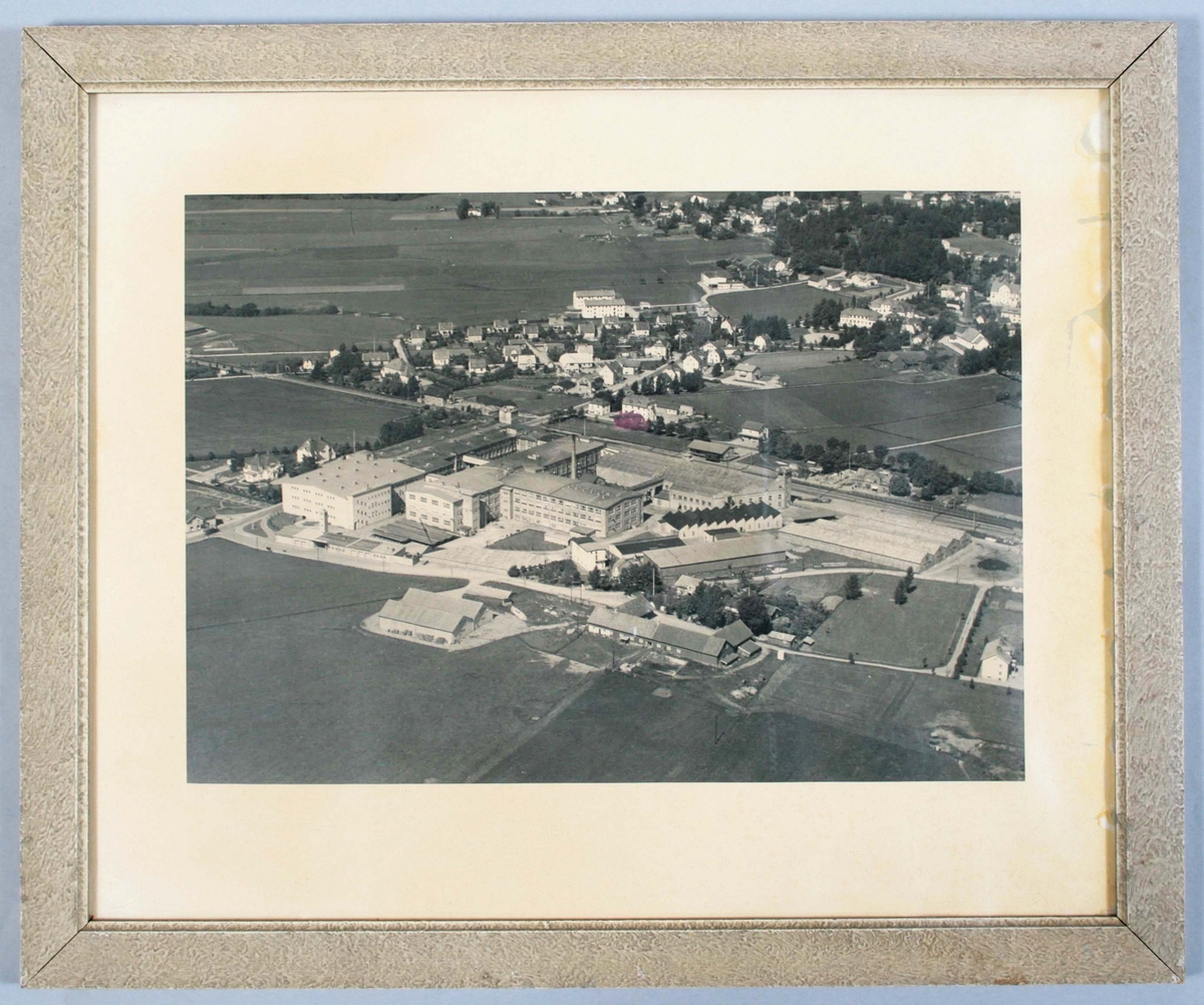 Inramat, svartvitt flygfotografi över fabriken i Kungsfors. Träram med grå marmorering. Bakstycke av spånplatta. Fuktskador. Proveniens Kungsfors Fabriker, Skene.