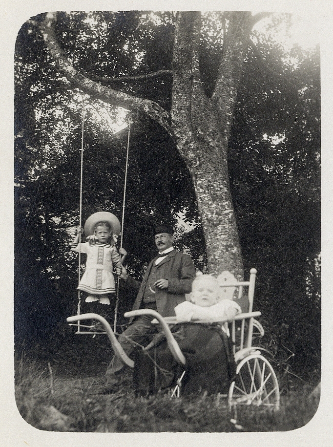 En okänd man med en flicka som står på en gunga och en baby, utomhus. Ca 1910.