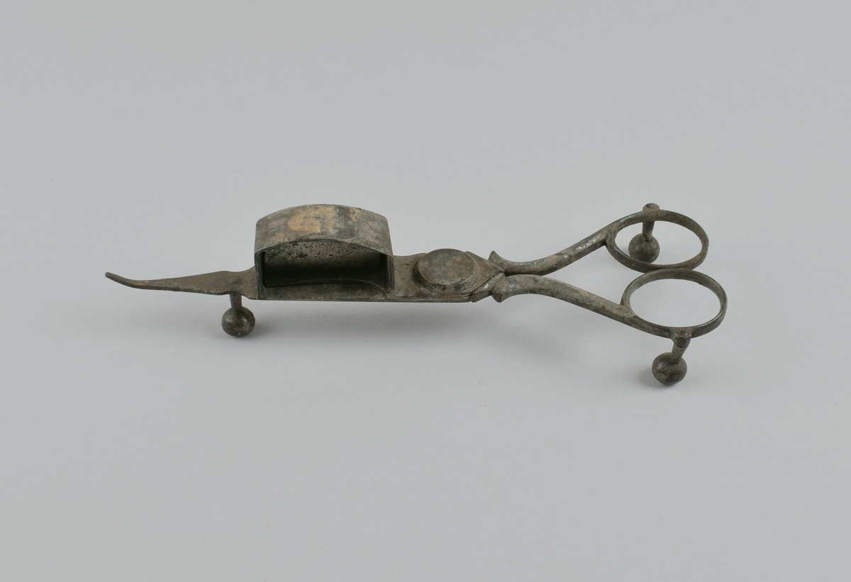 Saks med tre kuleben og liten beholder på ene bladet. Ble brukt til å kutte veke på levende lys, der veken brente senere enn talglyset smeltet.
