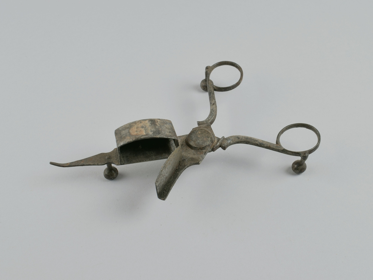 Saks med tre kuleben og liten beholder på ene bladet. Ble brukt til å kutte veke på levende lys, der veken brente senere enn talglyset smeltet.
