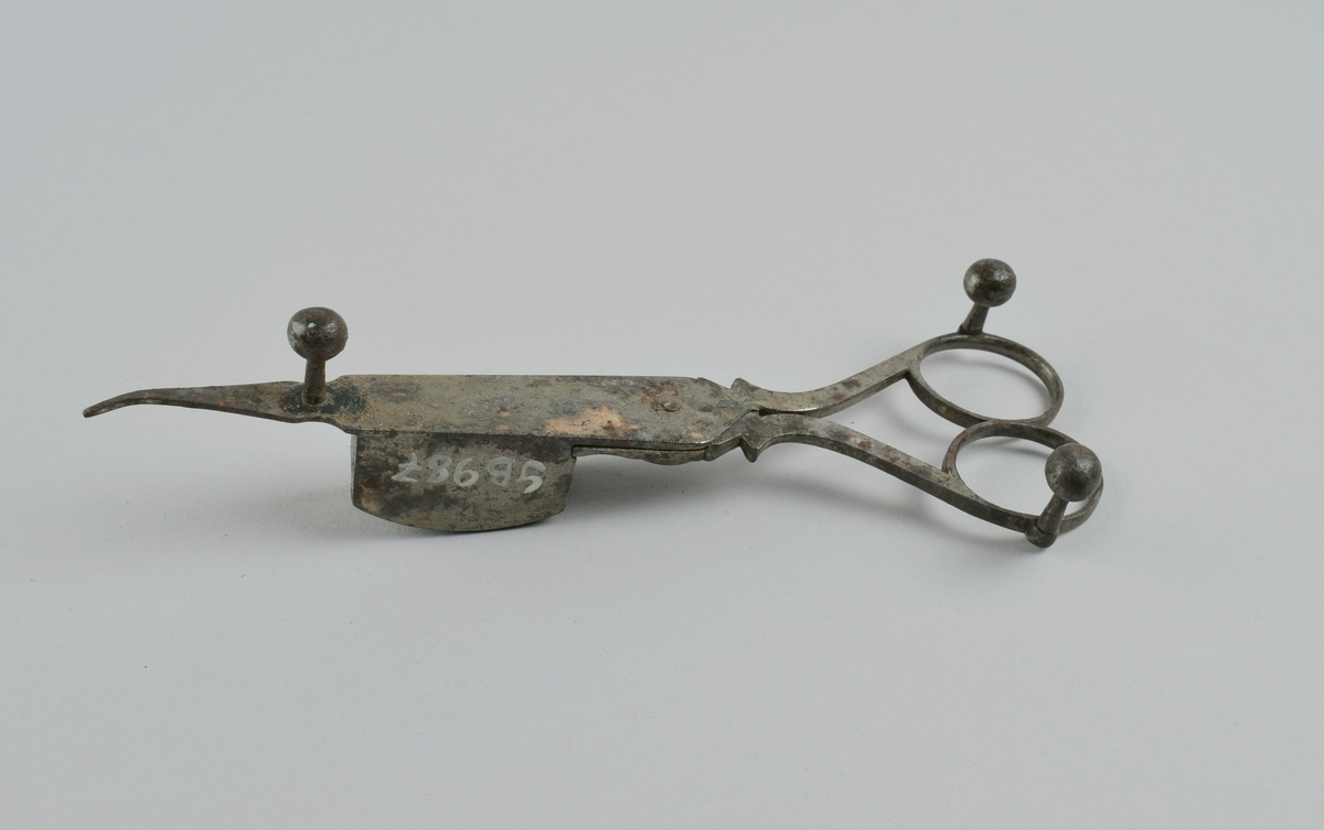 Saks med tre kuleben og liten beholder på ene bladet. Ble brukt til å kutte veke på levende lys, der veken brente senere enn talglyset smeltet.
