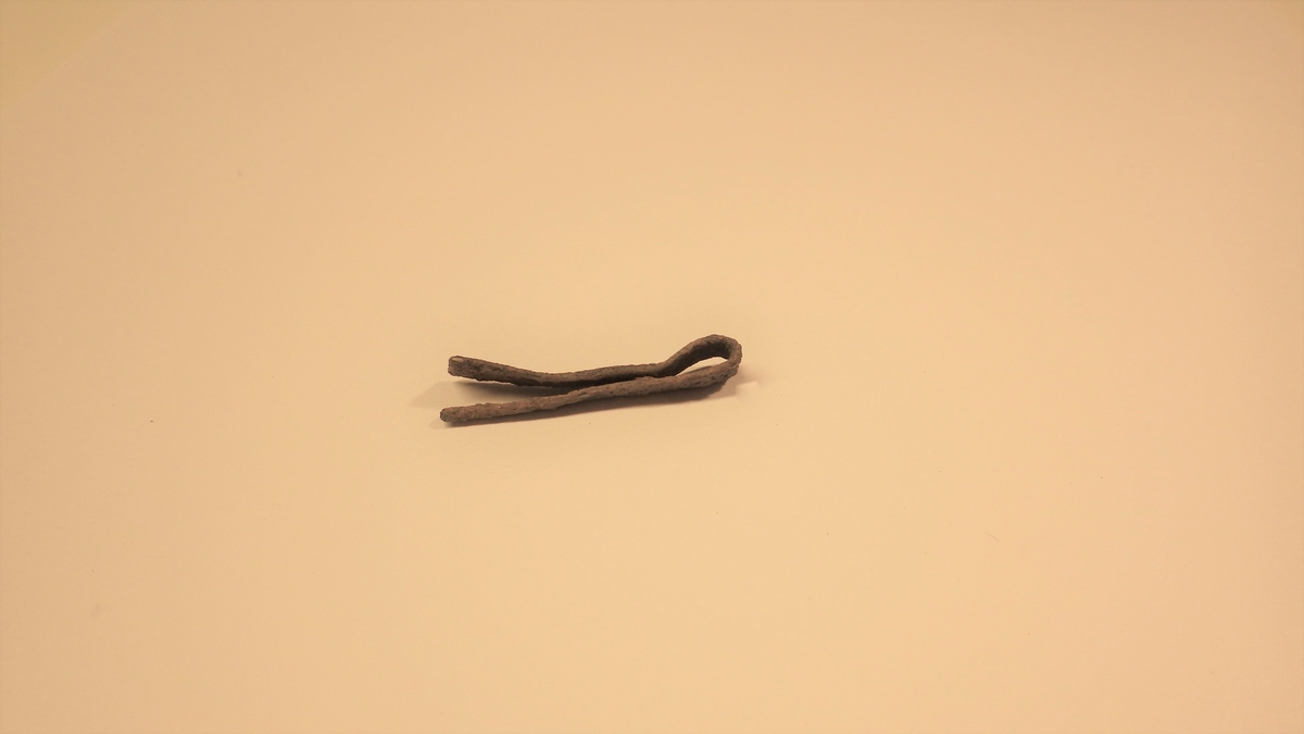 MÅL: L. 3, 2 CM, ST. B. 0, 6 CM, CA. 1 MM TYKK, AVSMALNENDE PLATE SOM ENDER I EN SPISS. OMBØYD.
