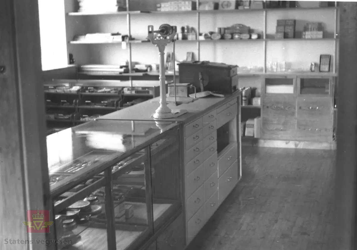 5 bilder av Blindheimsvik landhandel som ble flyttet til Norsk vegmuseum i 1995.

Blindheimsvik landhandel ble bygget i 1950 på Vigra i Giske kommune i Møre og Romsdal og var i drift som butikk frem til 1970 og som bolighus til 1992. Butikken ble drevet av Olav og Olga Blindheimsvik.

Norsk vegmuseum fikk tilbud om å kjøpe stedet med våningshus, butikk og uthus. Det ble tatt befaring i 1994 og høsten 1995 ble bygningene med alt interiør fotodokumentert slik det sto på Vigra. Alt interiøret ble pakket ned og fraktet i containere til Norsk vegmuseum. Alle bygningsdeler ble merket før det ble tatt ned. Murvegger og piper ble ikke flyttet, men revet. 

9. juni 2007 ble Blindheimsvik landhandel, leilighet og uthus gjenåpnet på Norsk vegmuseum. Ansvarlig for flytting og gjenreising var: Aslak Stø, Magnar Jevnehagen, Dagfinn Sveen og Per Stø.

(Kilde: Norsk vegmusum)

Bilde 1) Bildet viser Blindheimsvik landhandel, trolig fra 1950-tallet.
På bildet står en 1945 modell Ford lastebil. Lastebilen hører til bygningene. 
På bildet står også en Oldsmobile 1938 modell parkert. (Informant Ivar E. Stav)
Foran står 3 barn, en jente og to gutter. (Foto: Ukjent fotograf.)
Bilde 2) Bildet viser innevendig interiør slik butikken opprinnelig var. (Foto: Ukjent fotograf. )
Bilde 3 og 4) Blindheimsvik  landhandel med uthus slik den framstår i dag ved Norsk vegmuseum. På ene bildet står Ford lastebilen. (Foto: Ole A. Flatmark.)
Bilde 5) Bildet viser et eksempel på vareutvalget i butikken på Norsk vegmuseum (Foto: Ole A. Flatmark.)