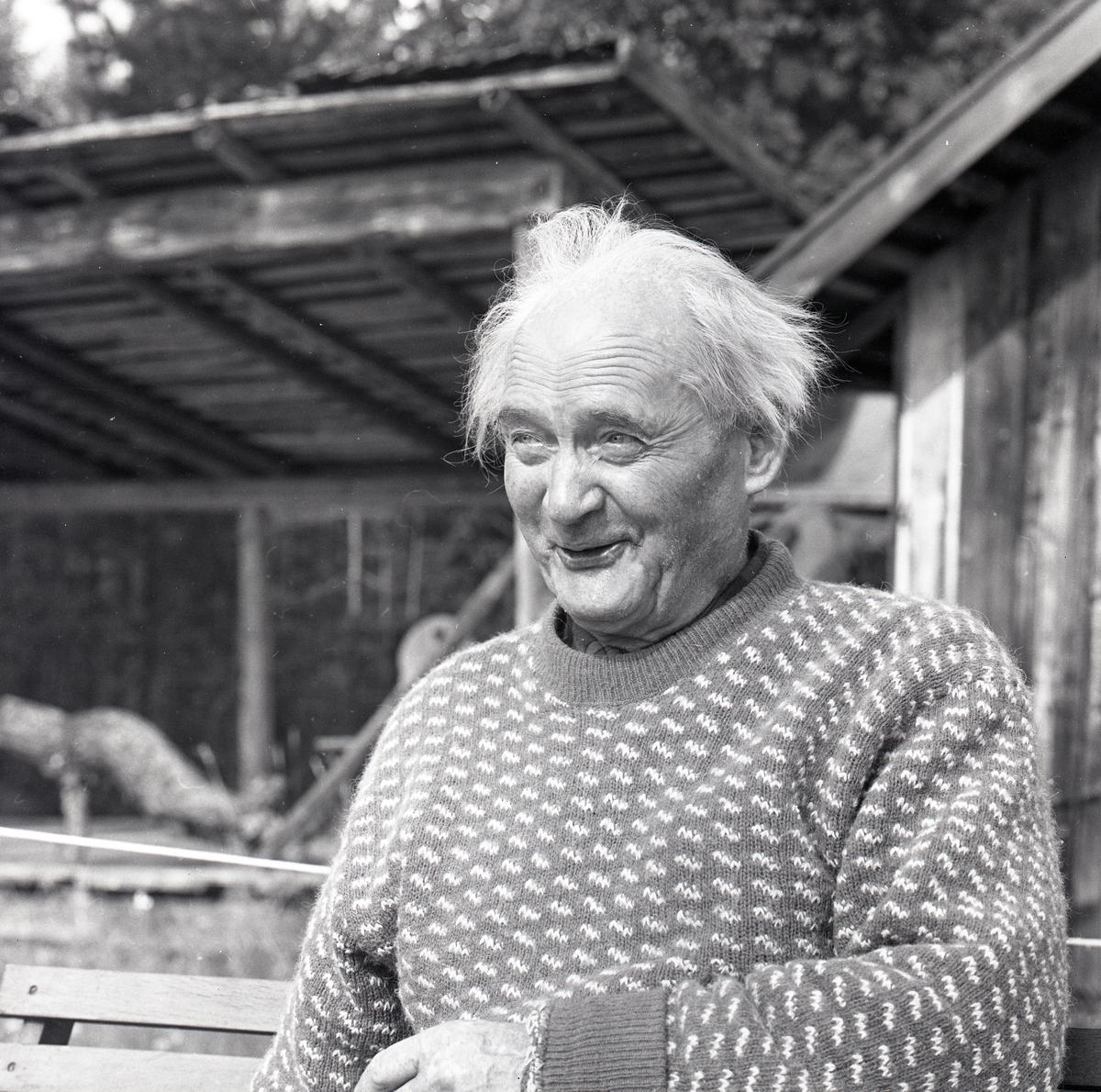 Författaren Albert Viksten sitter vid ett bord utomhus framför en träbyggnad. Han ler och berättar fiskehistorier, 19 augusti 1962.