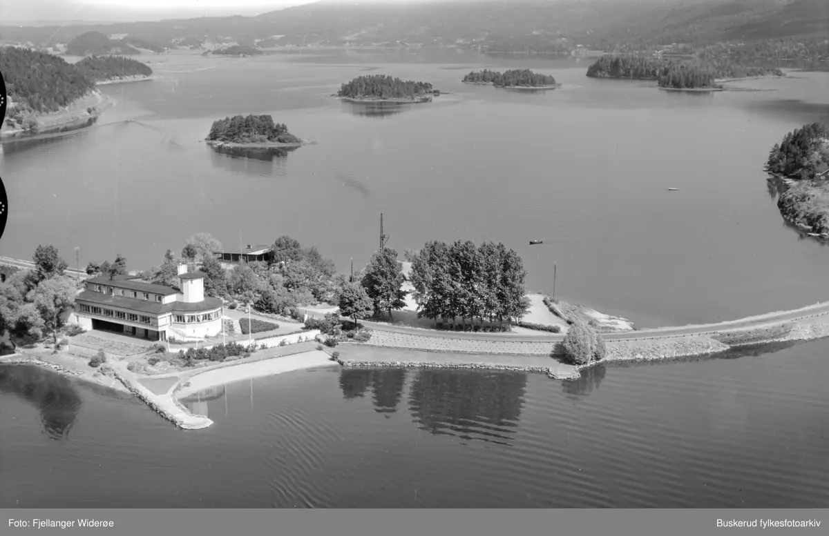 Sundøya fjordrestaurant. Ble bygget i 1938 og er nå revet.  Sundøya er en av to småøyer som ligger i Kroksundet, mellom Steinsfjorden og Tyrifjorden, i Hole kommune, Viken. I bakgrunnen ser vi Steinsfjorden med Pålsøya, Amundsøya, Tvehjulingen, Svinøya og Ulvøya på rad.
