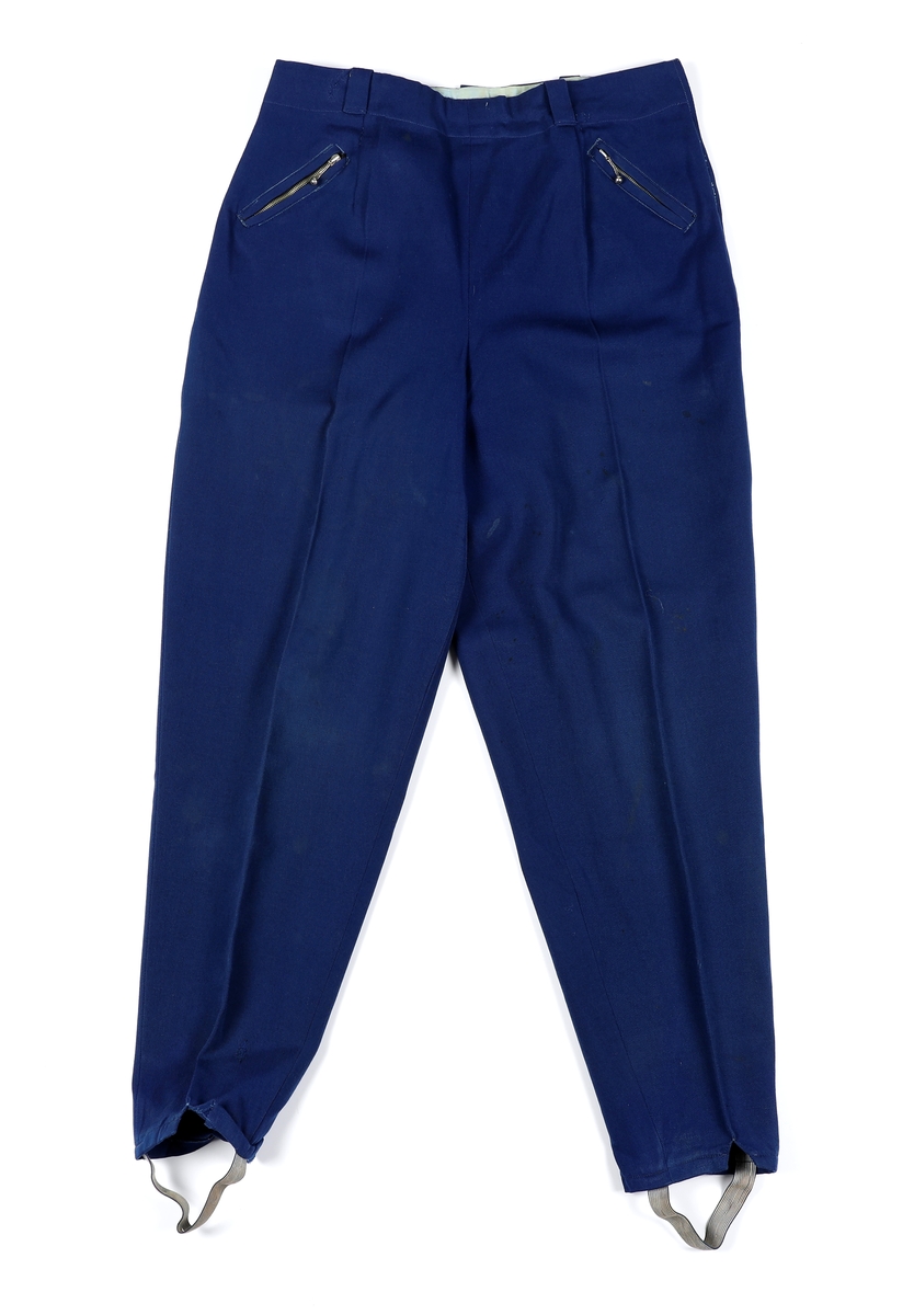 Overdel til drakt bestående av et kypertvevd blått bomullstoff brodert med ullgarn og med ermer og krage av lerretsvevd ull. Front og ermer har tinnknapper med støpt mønster. Det er hekter og trykknapper til å lukke med.
Buksa til drakta er av typen strekkbukse med press og strikk under beina. Den har glidelåslukning i siden og to lommer med glidelås i front.