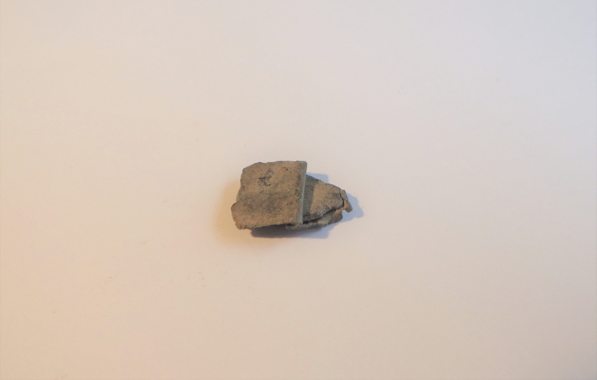 MÅL: L. 1, 6 CM B. 1, 3 CM, TYNN BRONSEPLATE, UREGELMESSIG FASONG. SAMMENBRETTET. GJENNOMGÅENDE FLATHAMRET NAGLE.