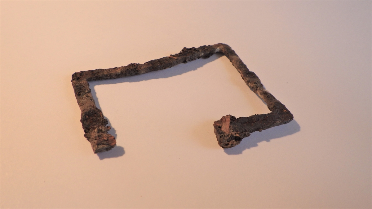 MÅL: B. 6, 0 CM H. 4, 4 CM, MULIG BRUKT TIL SKRIN. BRUKKET AV I ENE ENDEN. NOE UJEVNT, FLATT JERN, FORMET SOM ET REKTANGEL.
