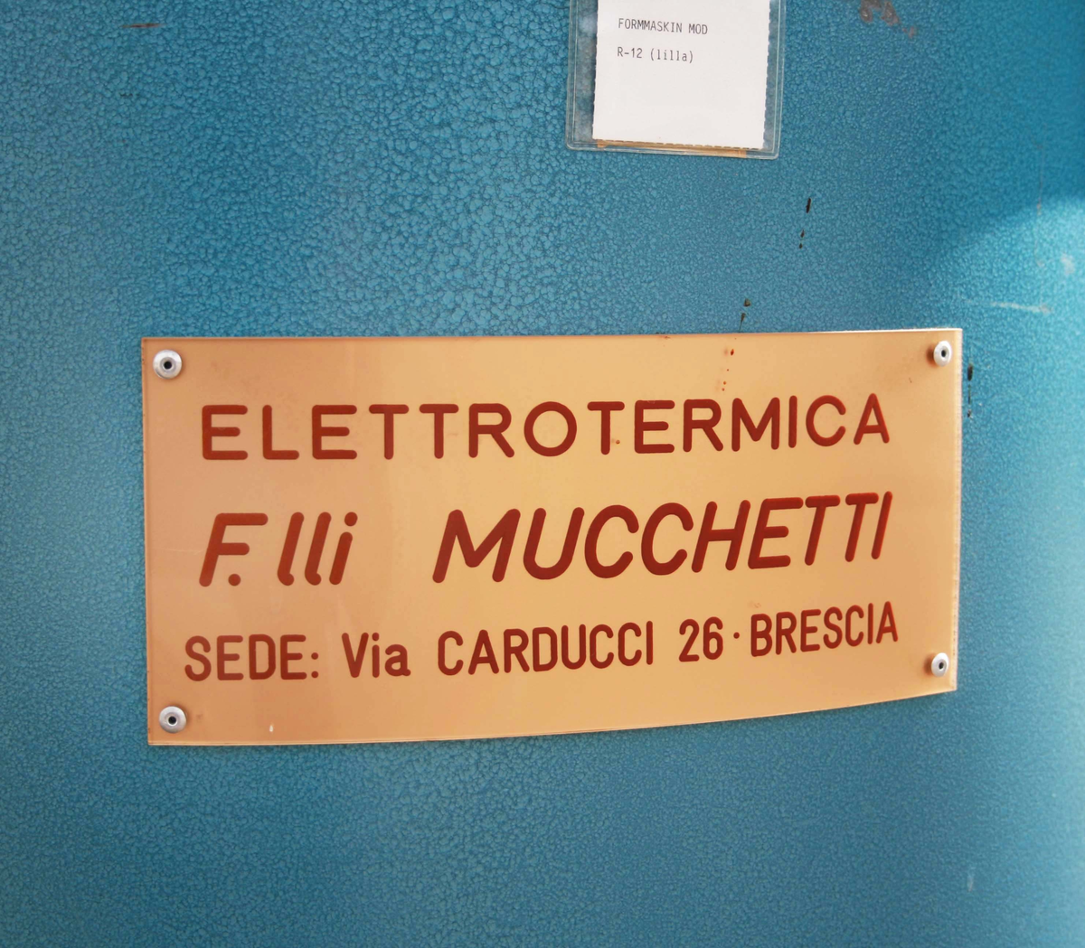 Strumpformare. Blålackerad, cylinderformad nederdel. Ovansidan, med rund roterande skiva och ställ för ett dussin strumpformar i aluminium. Märkt: Elettrotermica F.lli Muccetti, Brescia. Vagn med med strumpformar medföljer. Proveniens Seger Europe AB, Gällstad.

"Strumporna kom förfuktade till formningen i en vagn. Aluminiumformarna värmdes upp elektriskt. Formaren trär på strumporna och rättar till dem. När strumporna har roterat ett varv är de släta och torra. De tas av och skickas vidare till parning och paketering".

Funktion: För formning av strumpor