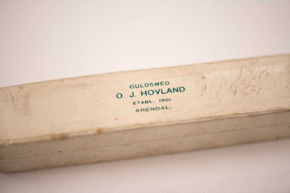 Nål med spirallrille, ender i treleddet lenke. I avlang eske fra Guldsmed 0. J. Hovland.