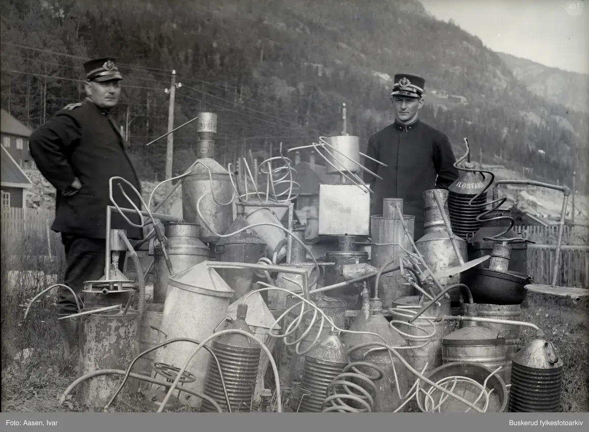 Lensmann Pedersen og sønn. Beslaglagte hjemmebrentutstyr fra anleggstiden. Bildet er tatt på sletta, foran lokomotivstallen i 1926