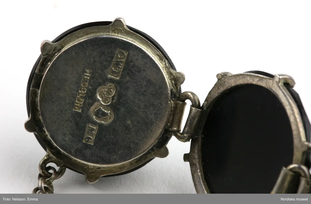 Armband av onyx och silver. Nio stycken runda fasettslipade onyxstenar infattade i silver. Fäste mellan två stenar med silvertunga som skjuts in i fäste (lösgörs genom att trycka ned metallpigg). Kedja mellan stenarna vid öppningen. Stämplar i silvret under en av stenarna vid fästet "CWT"/ kattfot (tre kronor)  / St Erik / M6 / Hedblom.".
/Leif Wallin 2021-09-24