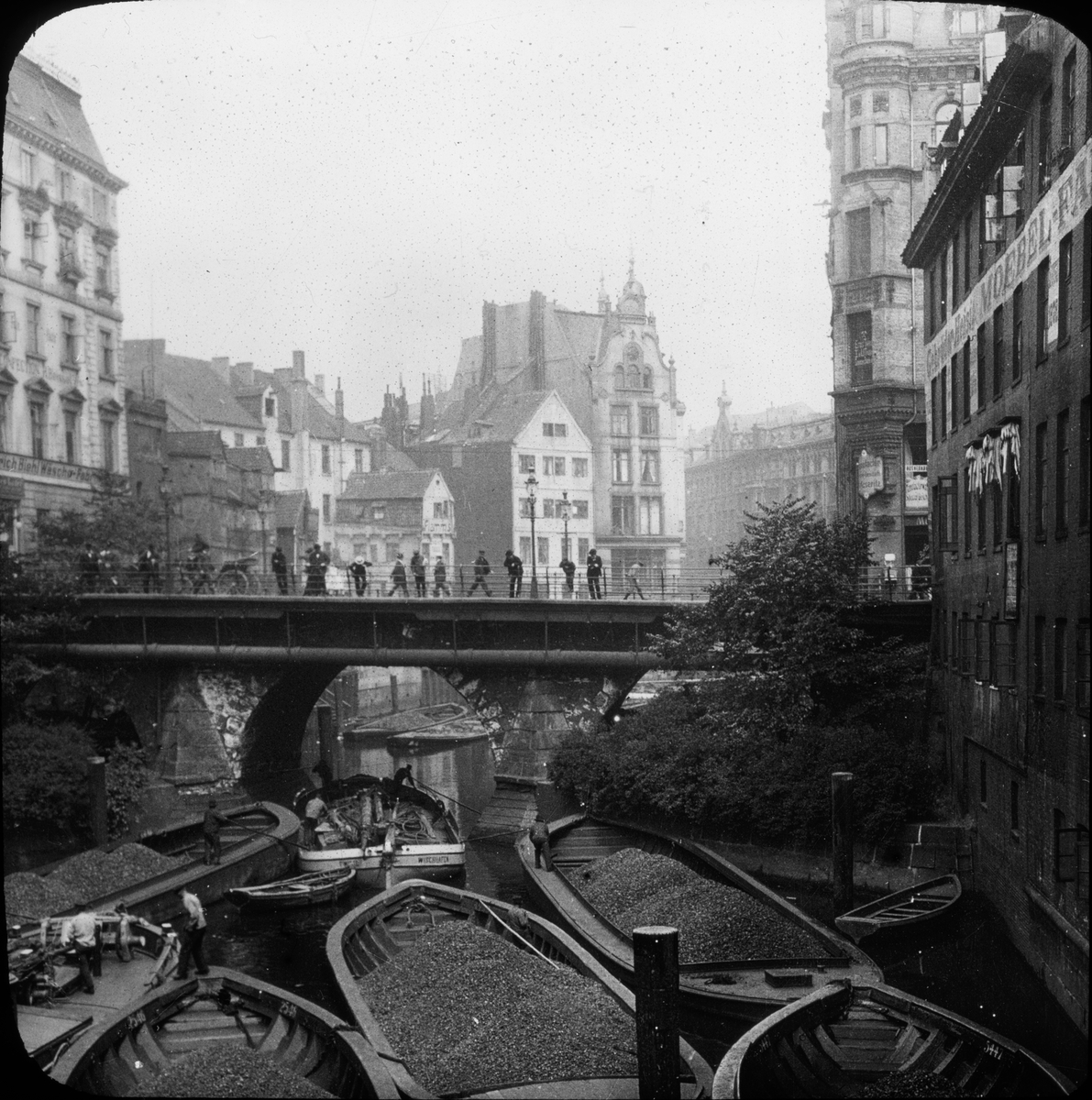 Skioptikonbild med motiv av arbete med lastade pråmar på kanal i Hamburg.
Bilden har förvarats i kartong märkt: Resan 1906. Hamburg 9.