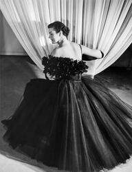 Mannekäng visar festplagg framför draperi i provrummet. Klän