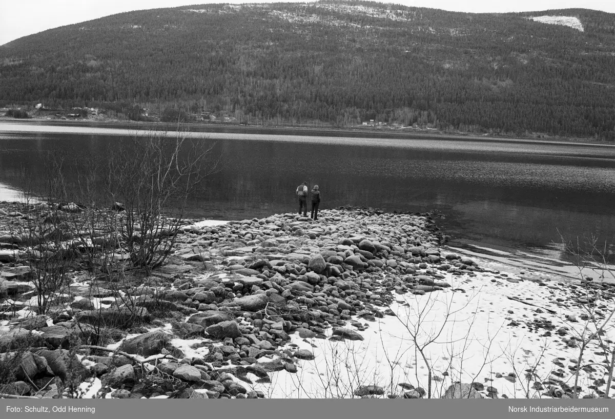 Kulturutvalget er på befaring på slippen ved Beita på Sigurdsrud. To mennesker står i strandsonen og ser ned i vannet Tinnsjø.