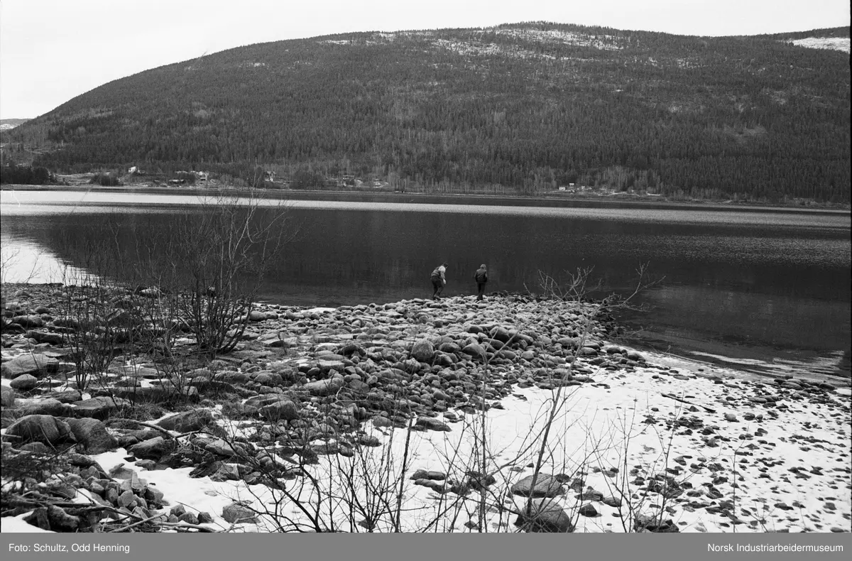 Kulturutvalget er på befaring på slippen ved Beita på Sigurdsrud. To mennesker står i strandsonen og ser ned i vannet Tinnsjø.