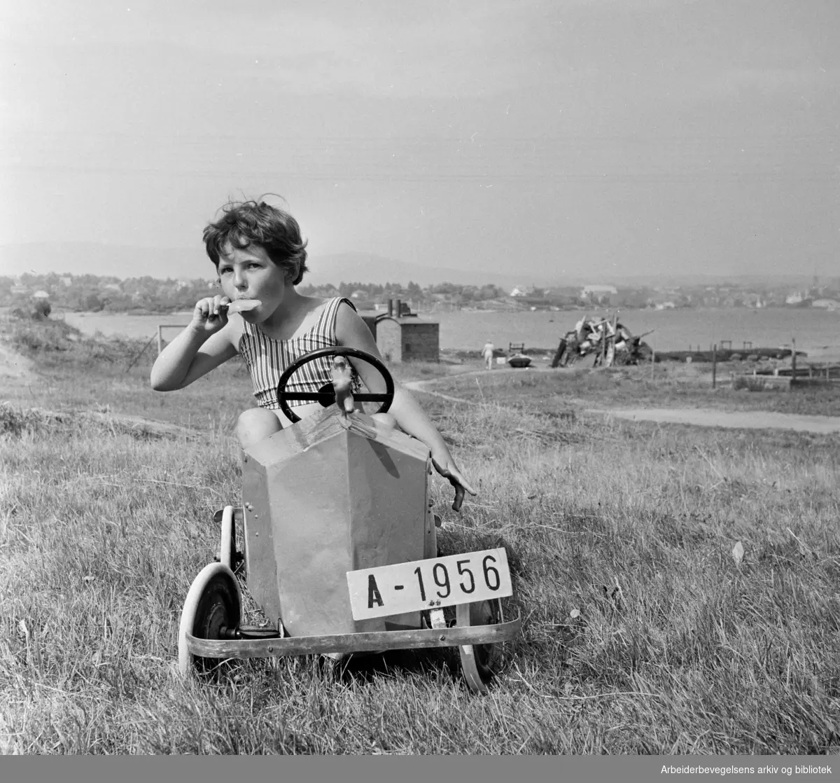 Nakholmen. Randi slapper av bak rattet med en ispinne. Juli 1966