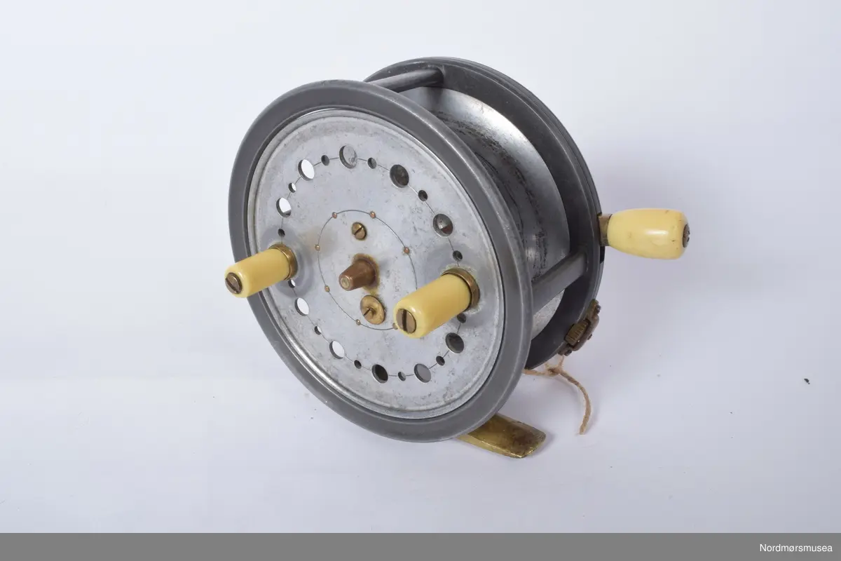 J. J. Walker Bampton kastesnelle, silextype. Modellen er kalt "The Utility". Slaterlatch for utløsing av spolen. På spolens framside to sveiver av ivorine. Snellehuset støpt i ett stykke med utløserarm med ivorineknopp på kanten mot baksiden. Glatt messingfot. Innvendig enkel klikktungebrems som løsnes av utløserarmen for kast. Justering av motstand med skrukott med riller på kanten mot baksiden under utløserarmen. Knotten beskyttet av bro, perforert spole.