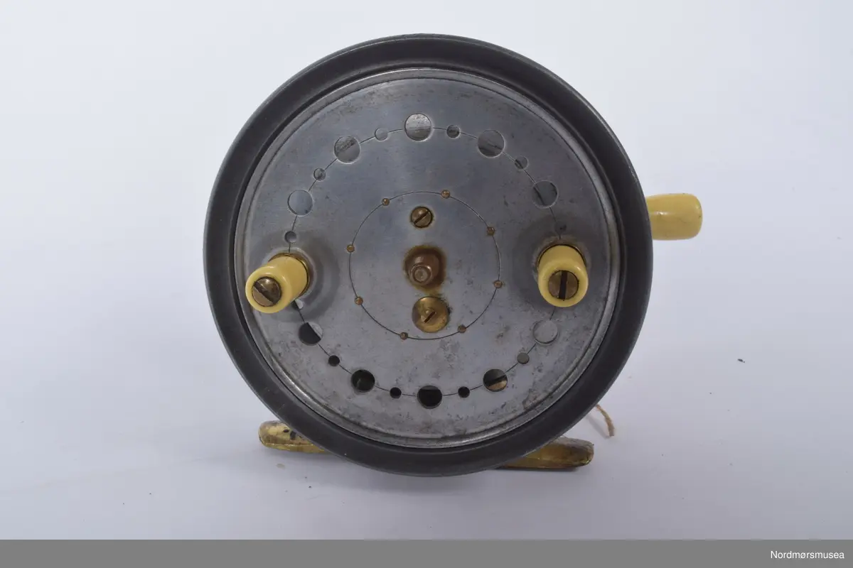 J. J. Walker Bampton kastesnelle, silextype. Modellen er kalt "The Utility". Slaterlatch for utløsing av spolen. På spolens framside to sveiver av ivorine. Snellehuset støpt i ett stykke med utløserarm med ivorineknopp på kanten mot baksiden. Glatt messingfot. Innvendig enkel klikktungebrems som løsnes av utløserarmen for kast. Justering av motstand med skrukott med riller på kanten mot baksiden under utløserarmen. Knotten beskyttet av bro, perforert spole.