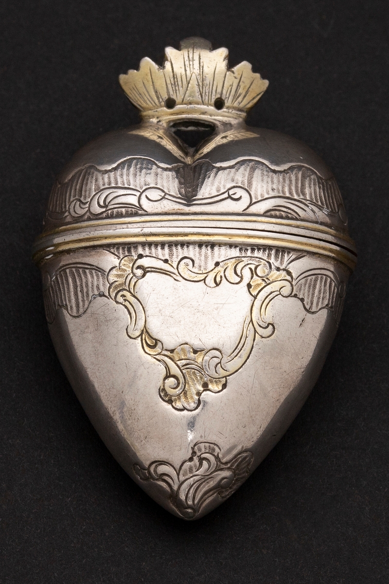 Hjerteformet luktevannshus i sølv uten fot. Delvis gjennombrutt, åpen, forgylt krone med strekgravyr på lokket. Gravert rokokko-ornamentikk på korpus; kartusj med rester av forgylling på forsiden. Forgylt kant rundt åpningen og innvendig forgylt.