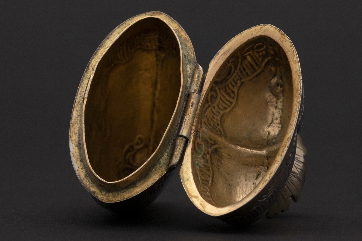 Hjerteformet luktevannshus i sølv uten fot. Delvis gjennombrutt, åpen, forgylt krone med strekgravyr på lokket. Gravert rokokko-ornamentikk på korpus; kartusj med rester av forgylling på forsiden. Forgylt kant rundt åpningen og innvendig forgylt.