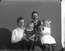 Sannolikt en familjegrupp: en kvinna, en man, två små barn och en hund, omfamnad av en flicka.