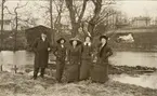 En medelålders man i paletå och hatt och en kvinna i promenaddräkt flankerar tre yngre kvinnor vid en åkant 
en vårvinterdag. Trol. i Åsedatrakten, ca 1915.