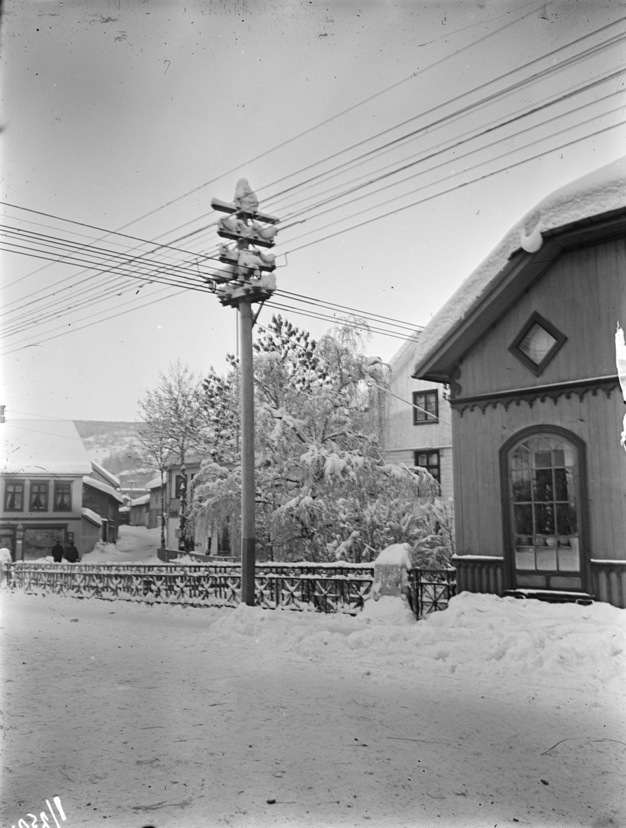 Mesna Kraftselskap. Stolpe og ledningskryss som stod ved Mesnabrua ved Lilletorget i Lillehammer. I forgrunnene er Storgata og Storgata 83,  i bakgrunnene ligger Gamlevegen