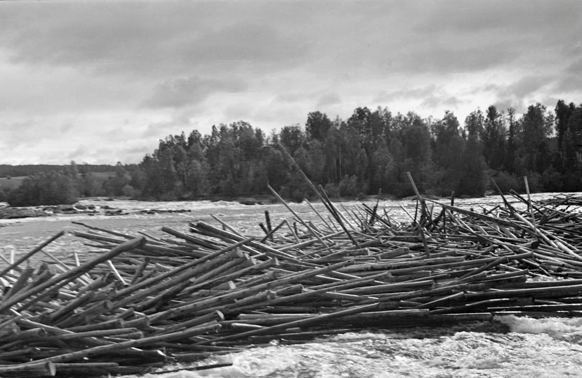 Tømmervase eller tømmerhaug i Funnefossen i Glomma. Dette fossefallet ligger lengst nord i Nes kommune på Romerike. Fotografiet er tatt på tvers av elveløpet, fra en posisjon ved elvebredden. I forgrunnen ser vi en langstrakt haug av fløtingstømmer som antakelig hadde byg seg opp på et av steinskjærene i fossen. Funnefossen har et samlet fall på bortimot 11 meter, fordelt over en strekning på drøyt 800 meter. Sentralt i fossen lå det en holme. Tømmerfløterne forsøkte, ved elvebredd. Funnefossen har et samlet fall på bortimot 11 meter, fordelt over en strekning på drøyt 800 meter. Bildet illustrerer hvordan tømmeret også her hadde lett for i binde seg i hauger eller vaser ved lav vannføring.