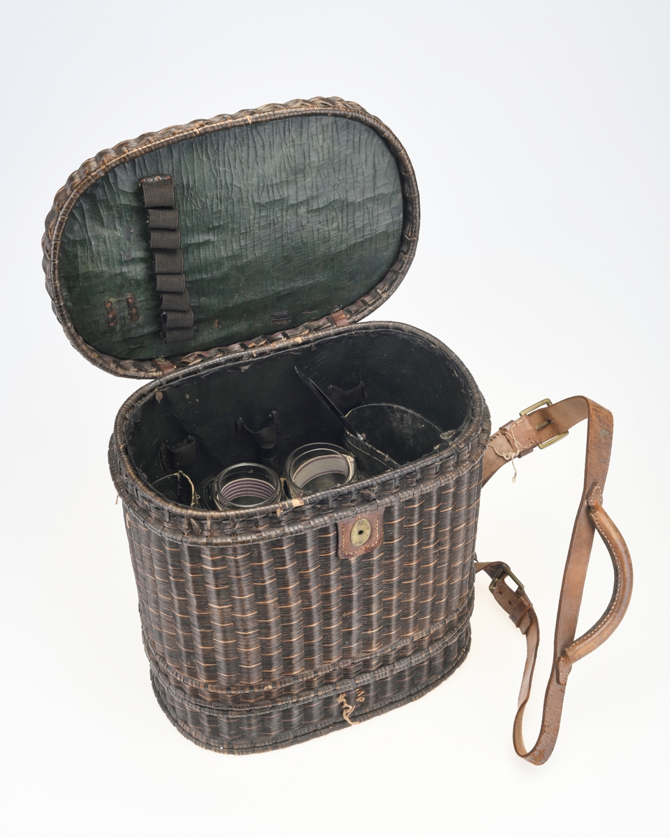 En piknikkurv med følgende innhold: 1 matboks, 2 større vannglass, 2 mindre vannglass, 4 hvite tallerkener, 4 kniver, 4 gafler og 1 beholder for salt/pepper. Kurven er flettet av pil eller lignende tre og er i ulik nyanser av brunt. Kurven er todelt, og i den nederste delen er det plass til matboksen, mens i den øverste delen det øvrige av piknikkutstyr. Beggel delene er foret med tesktil som er behandlet med granitol og deretter farget grønt. Langs kanten oppe (i begge delene) er det en svart tungekant av skinn. I den øverste delen av kurven er det festet strikk i lokket og i sidene i kurven for å feste utstyr. Det er også laget fire rom for å sette piknikkutstyr i. Rommene er laget av tekstil behandlet med granitol og farget grønn. Utvendig er det lærreimer som holder under- og overdel sammen samt fester lokket. De har spenner av messing og er dermed justerbare. I front er det et lite beslag med lås i messing. I den nederste deln av kurven er det plass til en oval matboks av blikk. Den har runde håndtak i hver side. Lokket er todelt og hengslet på midten slikk at lokkene åpnes mot midten. Inni boksen er det en skillevegg. Resten av utstyret er i "hovedkurven". Det er fire (vann)glass der i to forskjellige størrelser.  I de to største glassene er det en 1,5cm bred strikk som hindrer gnisning når de to mindre glassene er plassert i de to større. I tillegg er det fire hvite, enkle tallerkener. De har stempel på undersiden. Kurven innholder fire kniver og fire gafler. Knivene har avrundet blad av stål og svart trehåndtak. Gaflene har tre tinder av stål og svart trehåndtak. Til sist er det en beholder for salt og pepper. Den er av svart tre med dreid knopp på toppen. Skrur man av den øverste delen er det beholder for pepper. Skrur man av den nederste delen er det beholder for salt.