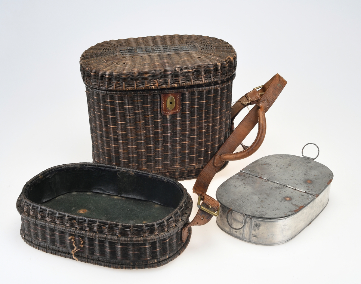 En piknikkurv med følgende innhold: 1 matboks, 2 større vannglass, 2 mindre vannglass, 4 hvite tallerkener, 4 kniver, 4 gafler og 1 beholder for salt/pepper. Kurven er flettet av pil eller lignende tre og er i ulik nyanser av brunt. Kurven er todelt, og i den nederste delen er det plass til matboksen, mens i den øverste delen det øvrige av piknikkutstyr. Beggel delene er foret med tesktil som er behandlet med granitol og deretter farget grønt. Langs kanten oppe (i begge delene) er det en svart tungekant av skinn. I den øverste delen av kurven er det festet strikk i lokket og i sidene i kurven for å feste utstyr. Det er også laget fire rom for å sette piknikkutstyr i. Rommene er laget av tekstil behandlet med granitol og farget grønn. Utvendig er det lærreimer som holder under- og overdel sammen samt fester lokket. De har spenner av messing og er dermed justerbare. I front er det et lite beslag med lås i messing. I den nederste deln av kurven er det plass til en oval matboks av blikk. Den har runde håndtak i hver side. Lokket er todelt og hengslet på midten slikk at lokkene åpnes mot midten. Inni boksen er det en skillevegg. Resten av utstyret er i "hovedkurven". Det er fire (vann)glass der i to forskjellige størrelser.  I de to største glassene er det en 1,5cm bred strikk som hindrer gnisning når de to mindre glassene er plassert i de to større. I tillegg er det fire hvite, enkle tallerkener. De har stempel på undersiden. Kurven innholder fire kniver og fire gafler. Knivene har avrundet blad av stål og svart trehåndtak. Gaflene har tre tinder av stål og svart trehåndtak. Til sist er det en beholder for salt og pepper. Den er av svart tre med dreid knopp på toppen. Skrur man av den øverste delen er det beholder for pepper. Skrur man av den nederste delen er det beholder for salt.