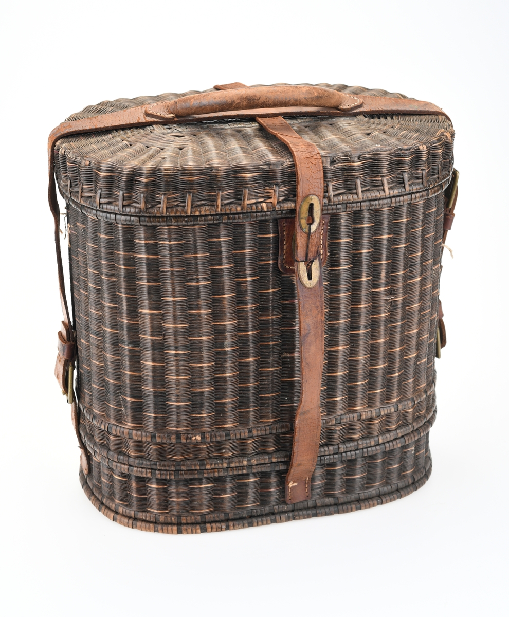 En piknikkurv med følgende innhold: 1 matboks, 2 større vannglass, 2 mindre vannglass, 4 hvite tallerkener, 4 kniver, 4 gafler og 1 beholder for salt/pepper. Kurven er flettet av pil eller lignende tre og er i ulik nyanser av brunt. Kurven er todelt, og i den nederste delen er det plass til matboksen, mens i den øverste delen det øvrige av piknikkutstyr. Beggel delene er foret med tesktil som er behandlet med granitol og deretter farget grønt. Langs kanten oppe (i begge delene) er det en svart tungekant av skinn. I den øverste delen av kurven er det festet strikk i lokket og i sidene i kurven for å feste utstyr. Det er også laget fire rom for å sette piknikkutstyr i. Rommene er laget av tekstil behandlet med granitol og farget grønn. Utvendig er det lærreimer som holder under- og overdel sammen samt fester lokket. De har spenner av messing og er dermed justerbare. I front er det et lite beslag med lås i messing. I den nederste deln av kurven er det plass til en oval matboks av blikk. Den har runde håndtak i hver side. Lokket er todelt og hengslet på midten slikk at lokkene åpnes mot midten. Inni boksen er det en skillevegg. Resten av utstyret er i "hovedkurven". Det er fire (vann)glass der i to forskjellige størrelser.  I de to største glassene er det en 1,5cm bred strikk som hindrer gnisning når de to mindre glassene er plassert i de to større. I tillegg er det fire hvite, enkle tallerkener. De har stempel på undersiden. Kurven innholder fire kniver og fire gafler. Knivene har avrundet blad av stål og svart trehåndtak. Gaflene har tre tinder av stål og svart trehåndtak. Til sist er det en beholder for salt og pepper. Den er av svart tre med dreid knopp på toppen. Skrur man av den øverste delen er det beholder for pepper. Skrur man av den nederste delen er det beholder for salt.