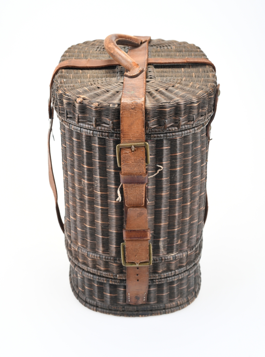 En piknikkurv med følgende innhold: 1 matboks, 2 større vannglass, 2 mindre vannglass, 4 hvite tallerkener, 4 kniver, 4 gafler og 1 beholder for salt/pepper. Kurven er flettet av pil eller lignende tre og er i ulik nyanser av brunt. Kurven er todelt, og i den nederste delen er det plass til matboksen, mens i den øverste delen det øvrige av piknikkutstyr. Beggel delene er foret med tesktil som er behandlet med granitol og deretter farget grønt. Langs kanten oppe (i begge delene) er det en svart tungekant av skinn. I den øverste delen av kurven er det festet strikk i lokket og i sidene i kurven for å feste utstyr. Det er også laget fire rom for å sette piknikkutstyr i. Rommene er laget av tekstil behandlet med granitol og farget grønn. Utvendig er det lærreimer som holder under- og overdel sammen samt fester lokket. De har spenner av messing og er dermed justerbare. I front er det et lite beslag med lås i messing. I den nederste deln av kurven er det plass til en oval matboks av blikk. Den har runde håndtak i hver side. Lokket er todelt og hengslet på midten slikk at lokkene åpnes mot midten. Inni boksen er det en skillevegg. Resten av utstyret er i "hovedkurven". Det er fire (vann)glass der i to forskjellige størrelser.  I de to største glassene er det en 1,5cm bred strikk som hindrer gnisning når de to mindre glassene er plassert i de to større. I tillegg er det fire hvite, enkle tallerkener. De har stempel på undersiden. Kurven innholder fire kniver og fire gafler. Knivene har avrundet blad av stål og svart trehåndtak. Gaflene har tre tinder av stål og svart trehåndtak. Til sist er det en beholder for salt og pepper. Den er av svart tre med dreid knopp på toppen. Skrur man av den øverste delen er det beholder for pepper. Skrur man av den nederste delen er det beholder for salt.