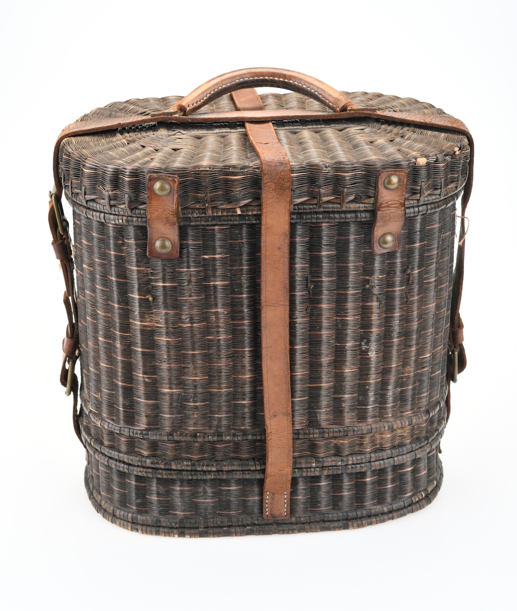 En piknikkurv med følgende innhold: 1 matboks, 2 større vannglass, 2 mindre vannglass, 4 hvite tallerkener, 4 kniver, 4 gafler og 1 beholder for salt/pepper. Kurven er flettet av pil eller lignende tre og er i ulik nyanser av brunt. Kurven er todelt, og i den nederste delen er det plass til matboksen, mens i den øverste delen det øvrige av piknikkutstyr. Beggel delene er foret med tesktil som er behandlet med granitol og deretter farget grønt. Langs kanten oppe (i begge delene) er det en svart tungekant av skinn. I den øverste delen av kurven er det festet strikk i lokket og i sidene i kurven for å feste utstyr. Det er også laget fire rom for å sette piknikkutstyr i. Rommene er laget av tekstil behandlet med granitol og farget grønn. Utvendig er det lærreimer som holder under- og overdel sammen samt fester lokket. De har spenner av messing og er dermed justerbare. I front er det et lite beslag med lås i messing. I den nederste deln av kurven er det plass til en oval matboks av blikk. Den har runde håndtak i hver side. Lokket er todelt og hengslet på midten slikk at lokkene åpnes mot midten. Inni boksen er det en skillevegg. Resten av utstyret er i "hovedkurven". Det er fire (vann)glass der i to forskjellige størrelser.  I de to største glassene er det en 1,5cm bred strikk som hindrer gnisning når de to mindre glassene er plassert i de to større. I tillegg er det fire hvite, enkle tallerkener. De har stempel på undersiden. Kurven innholder fire kniver og fire gafler. Knivene har avrundet blad av stål og svart trehåndtak. Gaflene har tre tinder av stål og svart trehåndtak. Til sist er det en beholder for salt og pepper. Den er av svart tre med dreid knopp på toppen. Skrur man av den øverste delen er det beholder for pepper. Skrur man av den nederste delen er det beholder for salt.