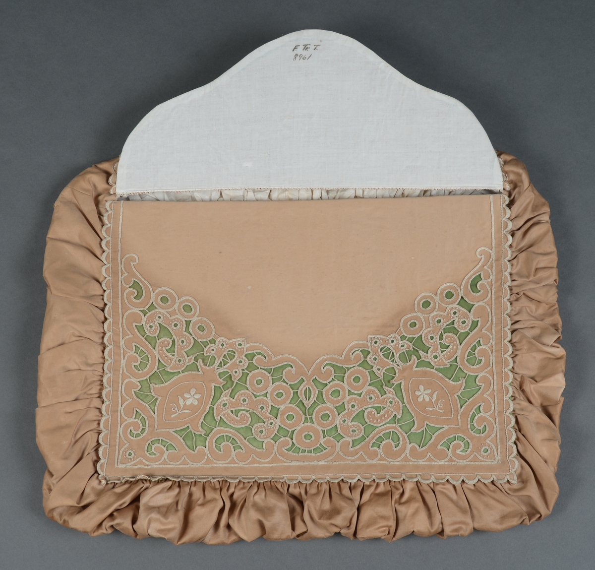 Rektangulær mappe med gjennomhullet broderi, "Venetiansk søm". Bunnen og lokkdelen er avstivet med en papp-plate, foret med hvitt chintzstoff. Sidene er av sammenrynket stoff som er sydd til bunnen og lokkdelene for hånd. Sidene er foret med samme stoff som bunn og lokkdelene. Under de broderte delene er det trekt med grønt silkestoff. Mappen inneholder 5 1/2 par mamelukker. 
Mamelukk 07, 1 singel, har brodert tungekant og engelskbroderi, håndsydd søm på utsiden og indresøm på innsiden av mamelukken, 2 knyttebånd.
Mamelukker 08, 1 par, har brodert tungekant og engelskbroderi, håndsydd, indresøm på ut- og innsiden av mamelukken, opprinnelig 2 knyttebånd på hver.
Mamelukker 09, 1 par, har innfelt mellomverk av kniplinger, 1 knyttebånd på utsiden i øvre kant, sømmene er håndsydde, indresøm på innsiden.
Mamelukker 10, 1 par, påsydd engelskbrodert kant, søm på innsiden av mamelukken, håndsydd, 2 knyttebånd på hver.
Mamelukker 11, 1 par, har brodert tungekant og engelskbroderi, håndsydd, indresøm på innsiden, opprinnelig 2 knyttebånd på hver.
Mamelukker 12, 1 par, påsydd engelskbrodert kant, søm på innsiden av mamelukken, håndsydd, 2 knyttebånd på hver.