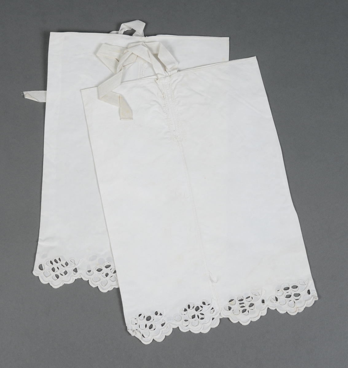 Rektangulær mappe med gjennomhullet broderi, "Venetiansk søm". Bunnen og lokkdelen er avstivet med en papp-plate, foret med hvitt chintzstoff. Sidene er av sammenrynket stoff som er sydd til bunnen og lokkdelene for hånd. Sidene er foret med samme stoff som bunn og lokkdelene. Under de broderte delene er det trekt med grønt silkestoff. Mappen inneholder 5 1/2 par mamelukker. 
Mamelukk 07, 1 singel, har brodert tungekant og engelskbroderi, håndsydd søm på utsiden og indresøm på innsiden av mamelukken, 2 knyttebånd.
Mamelukker 08, 1 par, har brodert tungekant og engelskbroderi, håndsydd, indresøm på ut- og innsiden av mamelukken, opprinnelig 2 knyttebånd på hver.
Mamelukker 09, 1 par, har innfelt mellomverk av kniplinger, 1 knyttebånd på utsiden i øvre kant, sømmene er håndsydde, indresøm på innsiden.
Mamelukker 10, 1 par, påsydd engelskbrodert kant, søm på innsiden av mamelukken, håndsydd, 2 knyttebånd på hver.
Mamelukker 11, 1 par, har brodert tungekant og engelskbroderi, håndsydd, indresøm på innsiden, opprinnelig 2 knyttebånd på hver.
Mamelukker 12, 1 par, påsydd engelskbrodert kant, søm på innsiden av mamelukken, håndsydd, 2 knyttebånd på hver.