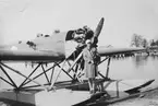 En flicka står på flygplan S 5 Heinkel He 5 på vatten. Flygplan med generator för elförsörjning.