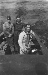 Tre militärer står i en motorbåt under färd. Vy ovanifrån. M