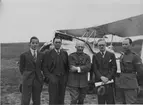 Gruppfoto av tre civilklädda män och två militärer framför flygplan Sk 9 på ett fält. I mitten major Axel Gyllenkrok, längst till höger Björn Bjuggren. 1930-tal.